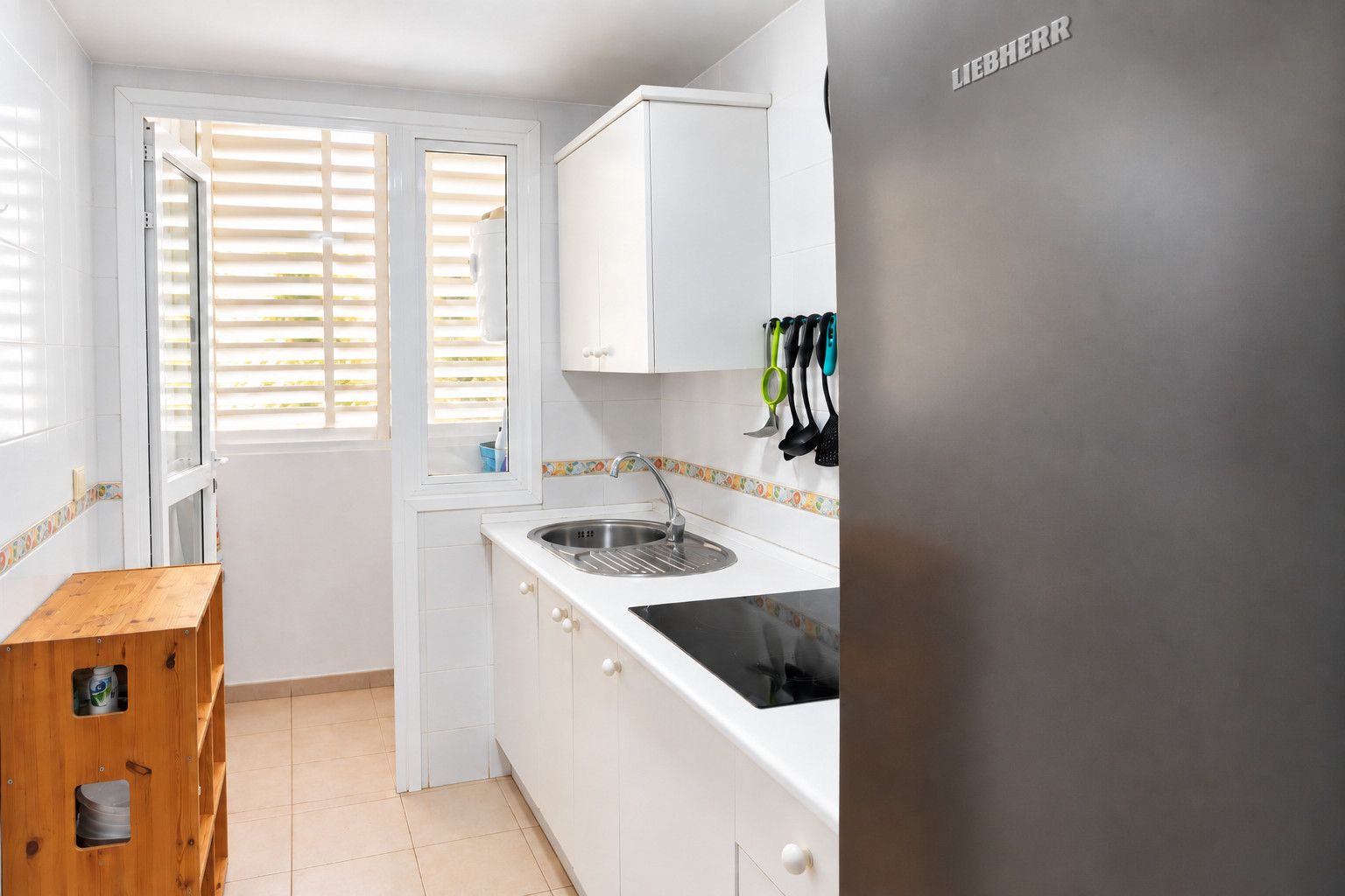 Una cocina con armarios blancos, un lavamanos de acero inoxidable y una ventana con persianas.