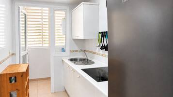 Una cocina con armarios blancos, un lavamanos de acero inoxidable y una ventana con persianas.