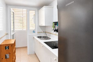 Een keuken met witte kastjes, een roestvrijstalen spoelbak en een raam met jaloezieën.