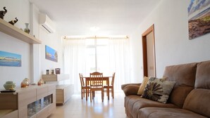 A living room with a brown sofa, a wooden dining table with chairs, a glass cabinet, and a painting on the wall. - - (Granadilla de Abona)