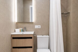 A bathroom with a wooden vanity, a toilet, a shower with a curtain, and a mirror.