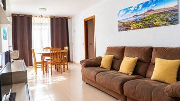 Una sala de estar con un sofá marrón, cojines amarillos, una mesa de comedor con sillas y un cuadro en la pared.
