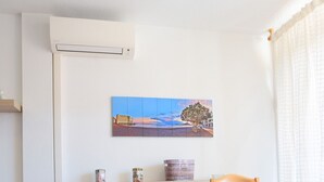 A dining area with a wooden table and chairs, a white air conditioning unit, a painting on the wall, and a window with curtains. - - (Granadilla de Abona)