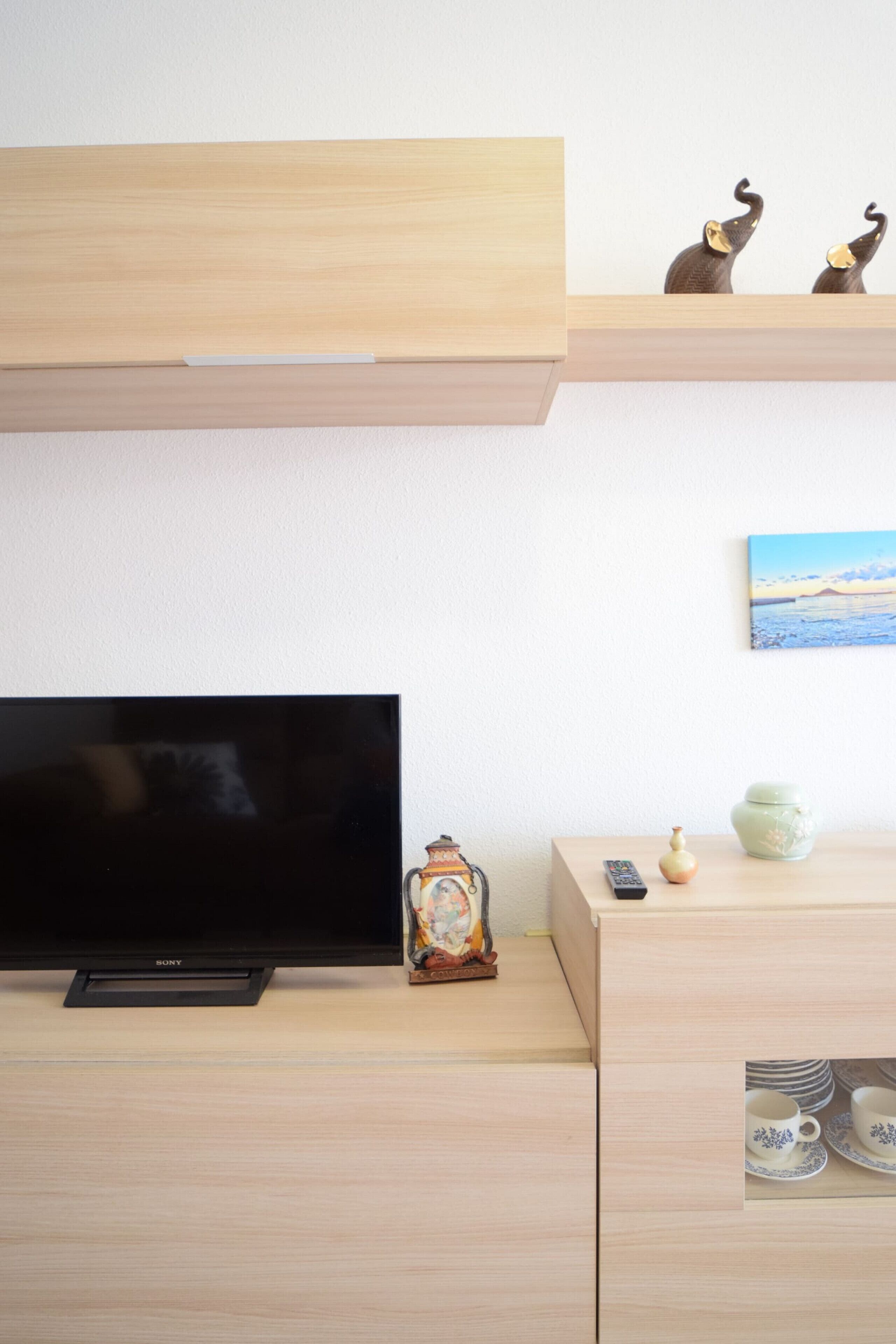 Un salón minimalista con un televisor de pantalla plana, un mueble de madera, adornos y un cuadro en la pared.