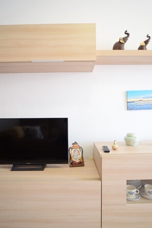 Un salon minimaliste avec un téléviseur à écran plat, un meuble en bois, des objets décoratifs et un tableau accroché au mur.