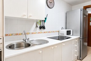 Una cocina con un lavamanos de acero inoxidable, armarios blancos, un microondas y un reloj en la pared.