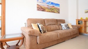 A living room with a brown sofa, a glass coffee table, and a painting on the wall. - - (Granadilla de Abona)