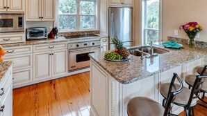 A kitchen with white cabinets, a stainless steel refrigerator, a built-in oven, a microwave, a toaster, and a granite countertop.