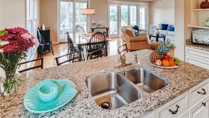 A kitchen with granite countertops, stainless steel sink, and a dining area with a table and chairs.
