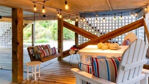 A wooden deck with a white table and chairs, string lights, and a view of greenery.