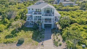 A multi-story beachfront house with a wooden deck and multiple balconies, surrounded by dense greenery. - Oceanview. Steps to South Beach • Stunning Sunset Views • Golf Carts Included • (Bald Head Island)