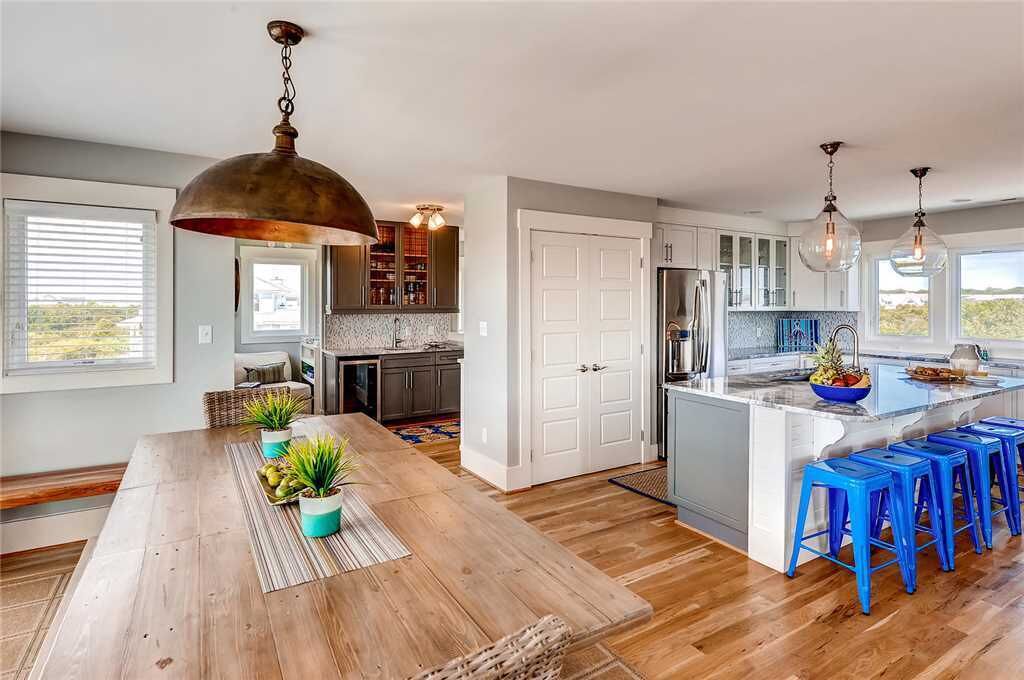 A spacious kitchen with a wooden dining table, blue bar stools, and a large island.