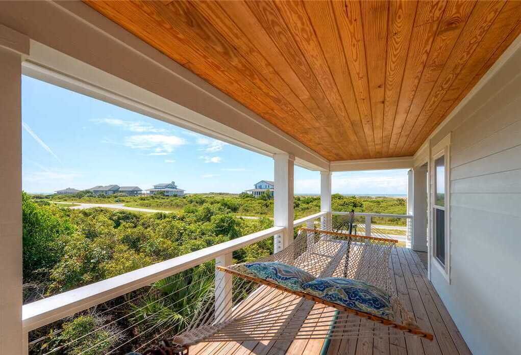 Una terraza de madera con una hamaca y vistas a un paisaje costero.
