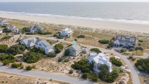 An aerial view of a coastal residential area with multiple houses, a beach, and a road.