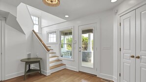 A spacious room with a wooden staircase, white walls, and a large door leading outside.