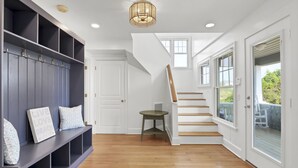 A modern interior with a wooden staircase, a bench with storage, and a view to the outdoors.