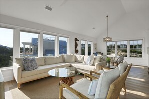 A spacious living room with a large sectional sofa, a glass coffee table, and a wicker chair.