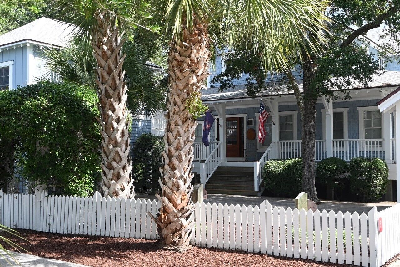 A two-story house with a white picket fence, a porch with steps, and a flag.