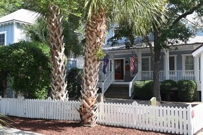 A two-story house with a white picket fence, a porch with steps, and a flag.
