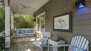 Eine überdachte Veranda mit weißen Adirondack-Stühlen, einer Bank mit gemusterten Kissen und einem gerahmten Schild an der Wand.