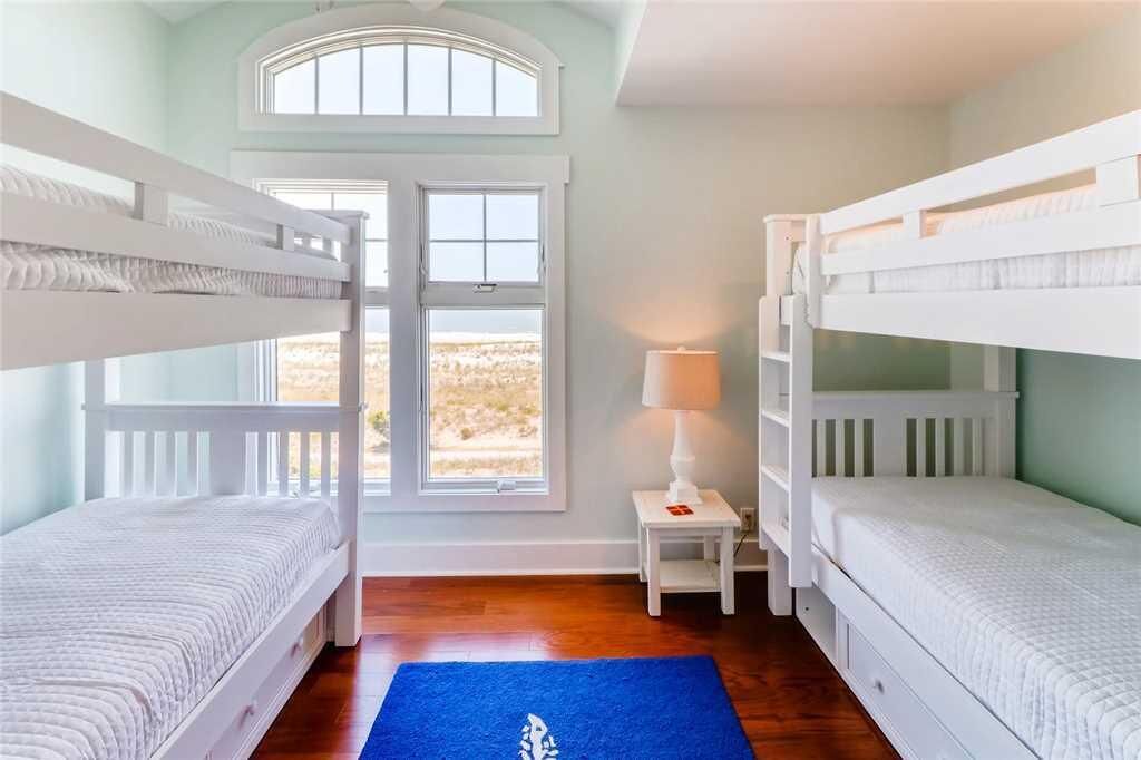 Une chambre avec deux lits superposés, une petite table de chevet avec une lampe et une grande fenêtre donnant sur l’extérieur.