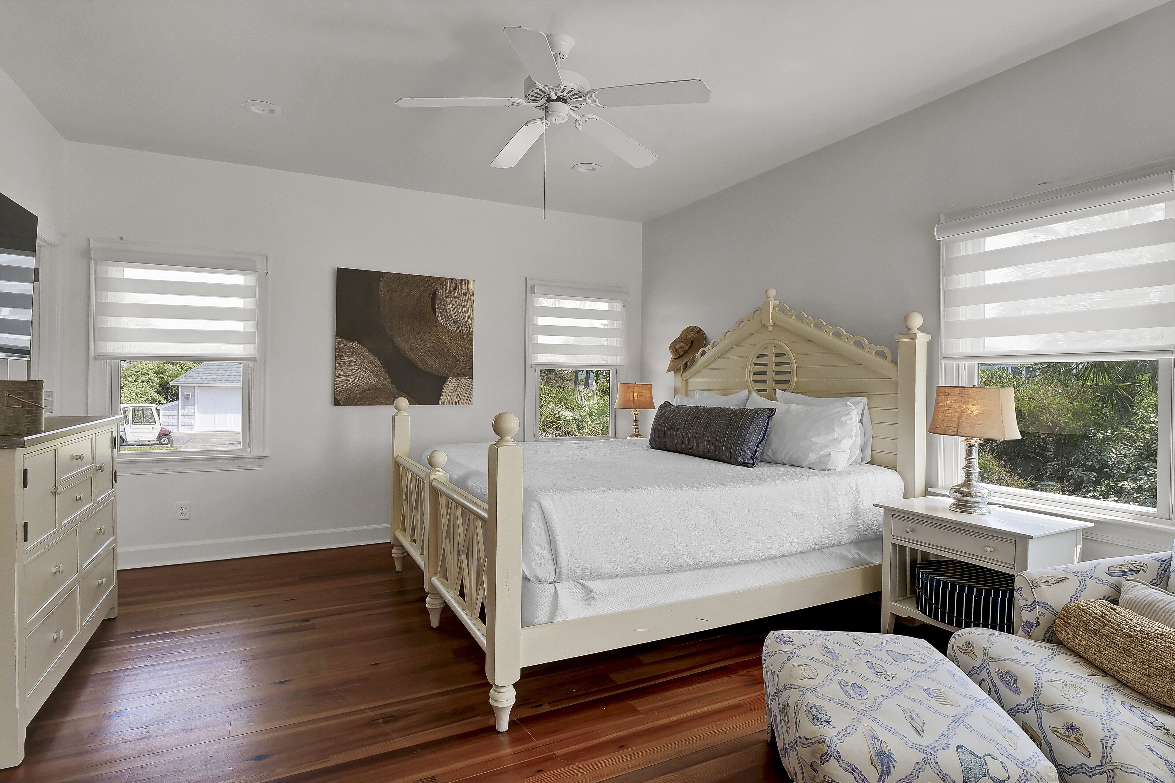 A bedroom with a white four-poster bed, a ceiling fan, and a nightstand with a lamp.