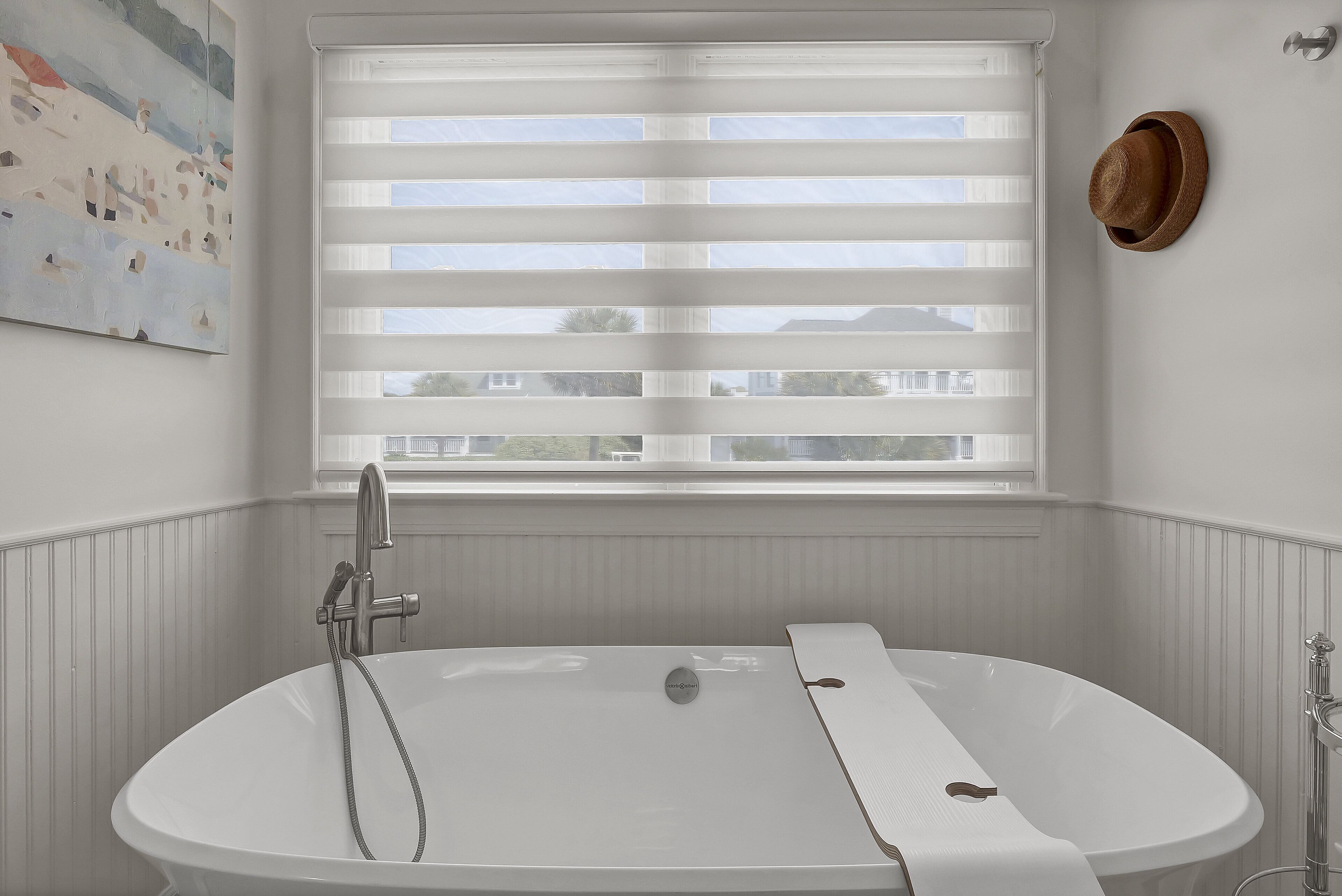 A bathroom with a freestanding bathtub, a window with blinds, and a wall-mounted hat.