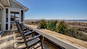 Eine Holzterrasse mit Stühlen mit Blick auf einen Strand.