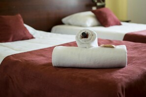 Quarto de hotel com duas camas, cada uma com colcha vermelha e almofadas brancas.