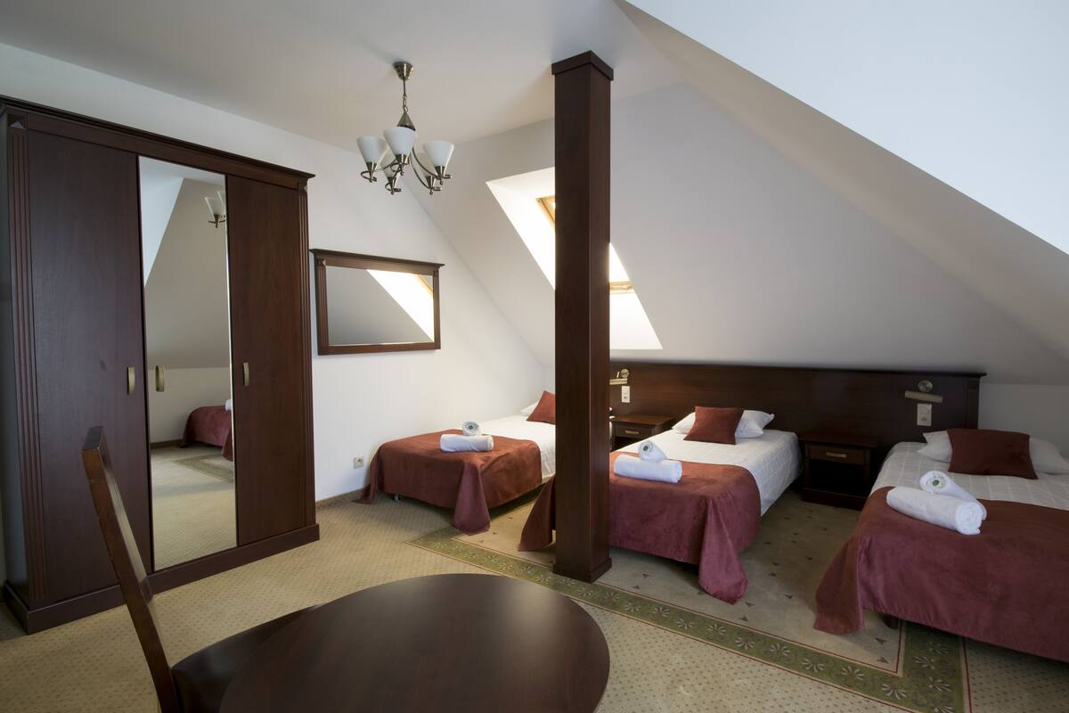 Habitación de hotel con dos camas individuales, un espejo grande, una araña y una mesa de comedor.
