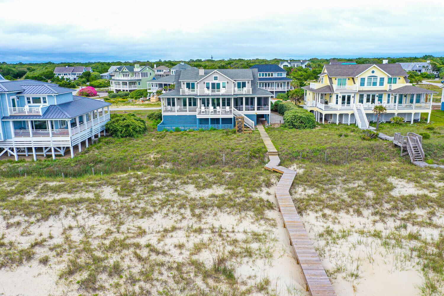 A coastal residential area with houses featuring large porches and a wooden boardwalk leading to the beach.