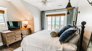 Een slaapkamer met een bed, een televisie, een dressoir en een balkon met gordijnen.
