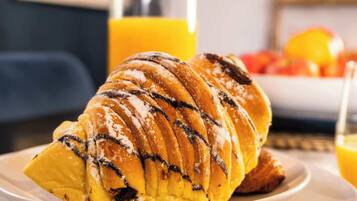 Een croissant op een bord, met een fles sinaasappelsap op de achtergrond.