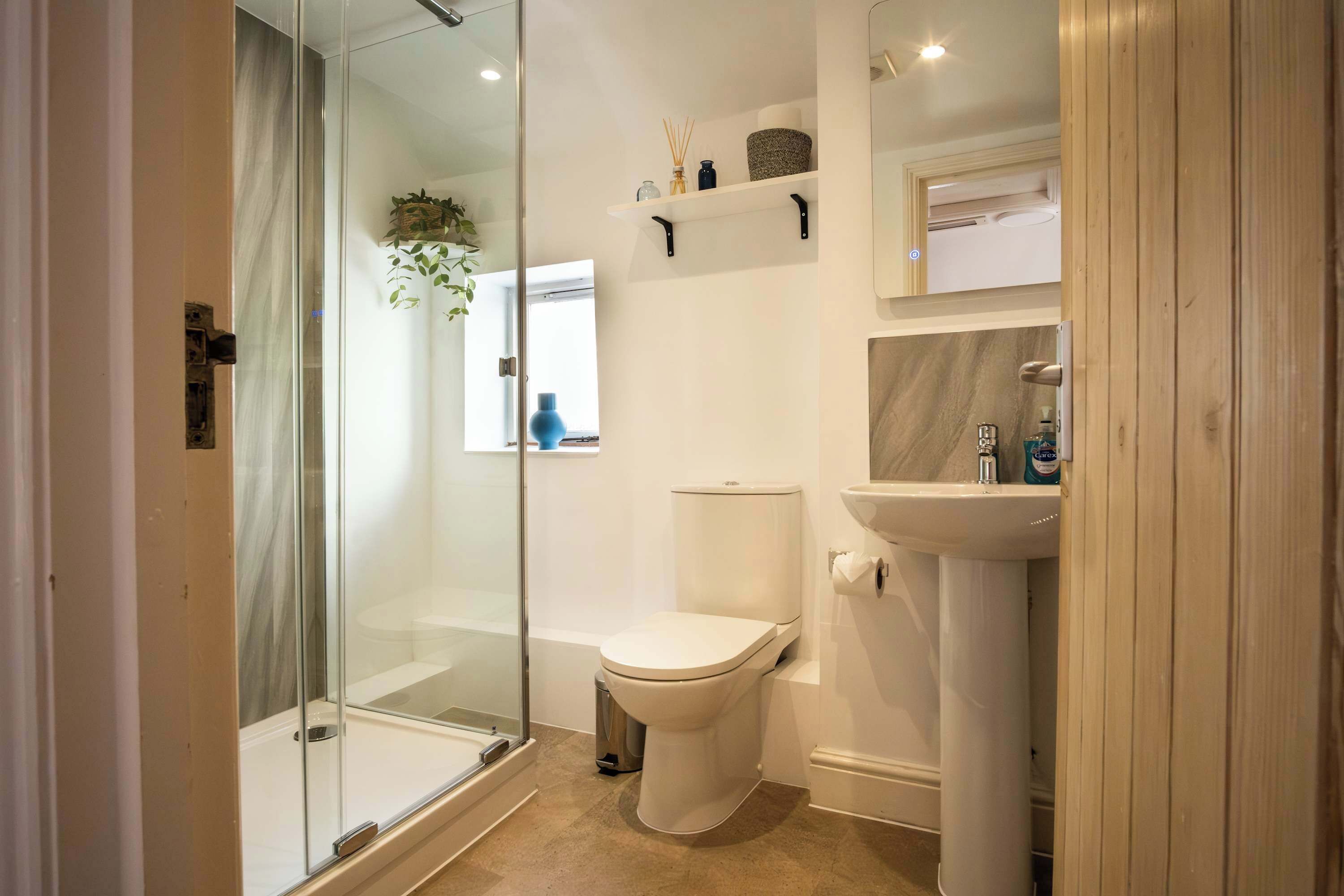 Een moderne badkamer met een douchecabine van glas, een toilet, een wastafel en een plank met toiletartikelen.