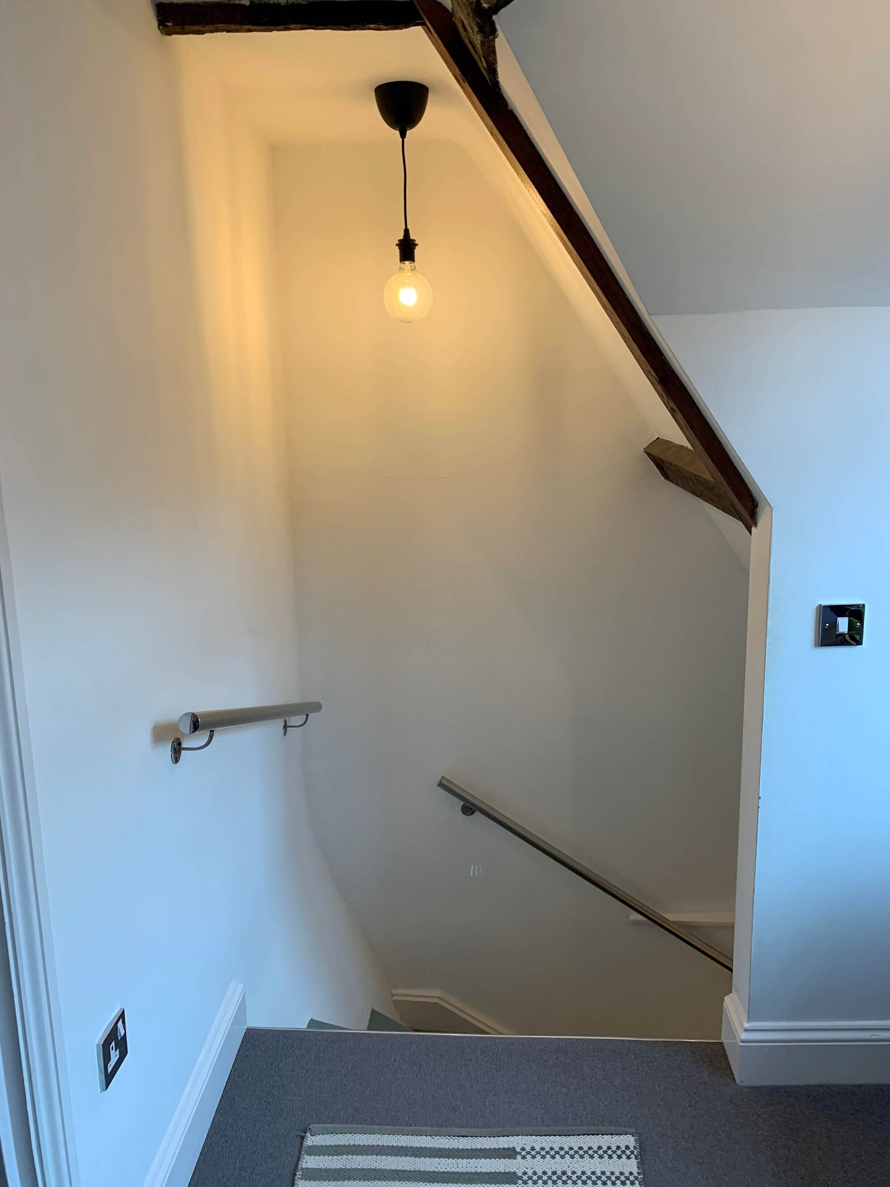 A staircase with a handrail, a light fixture, and a carpeted landing.