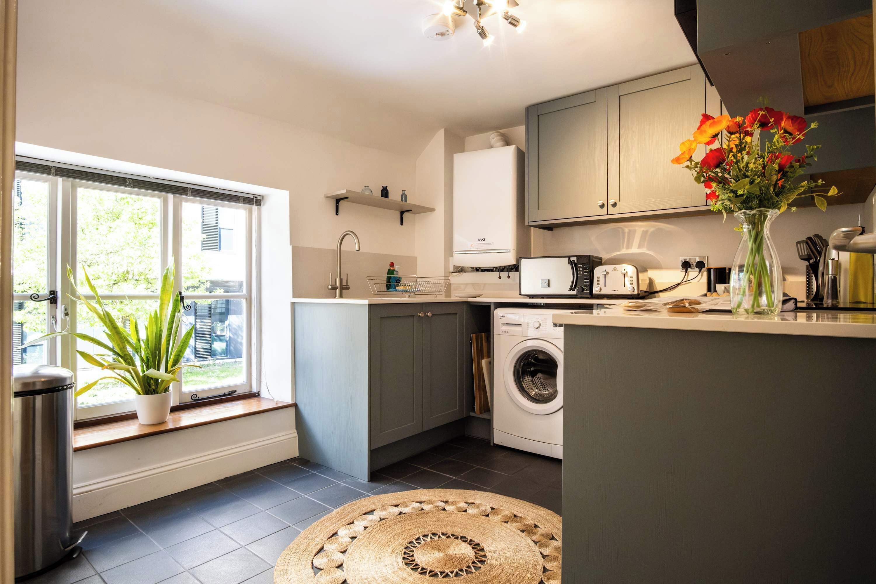 A compact kitchen with a washing machine, a sink, and a window with a plant.