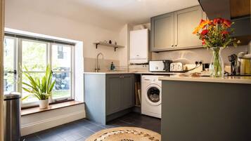 A compact kitchen with a washing machine, a sink, and a window with a plant.