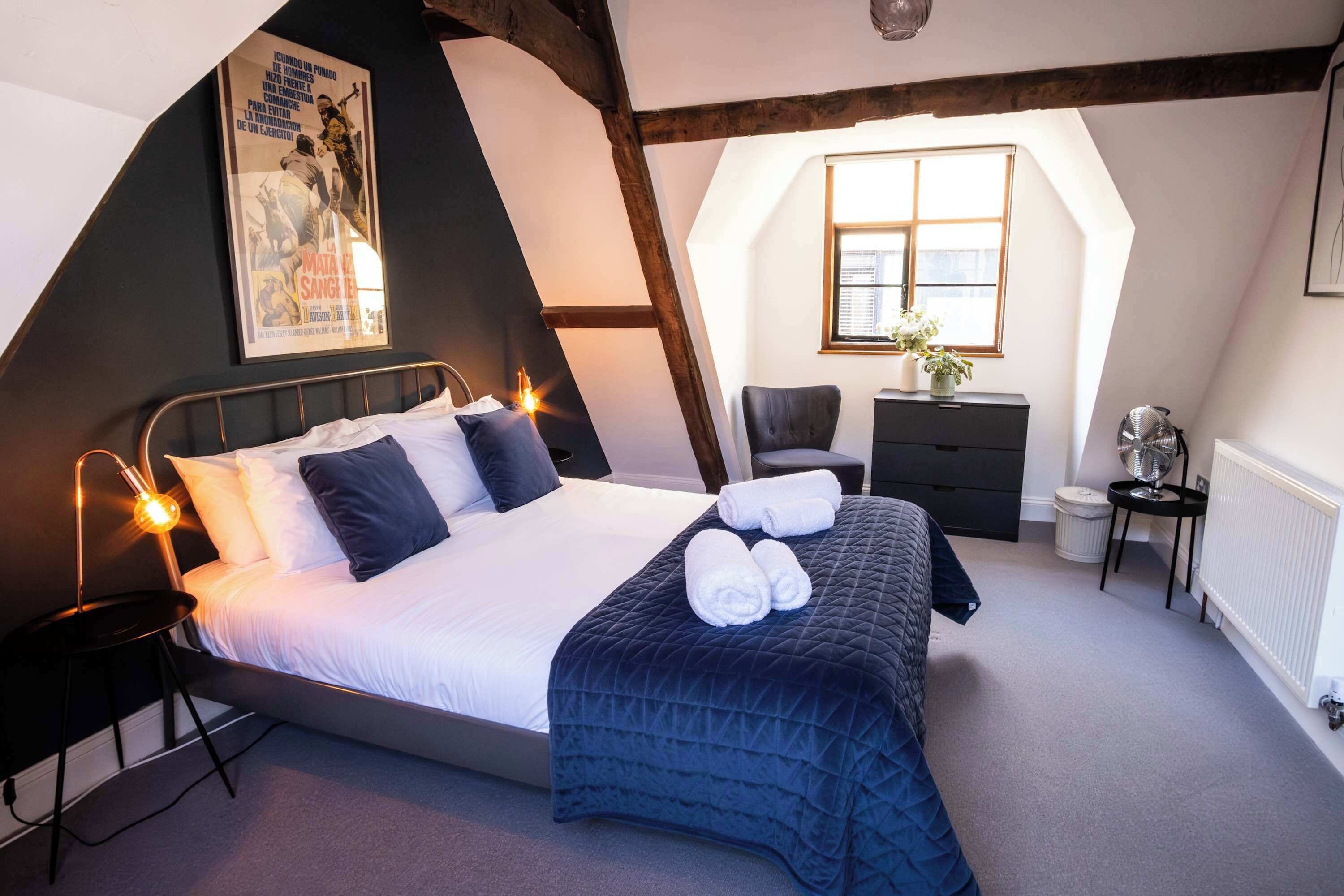 A bedroom with a bed, a desk, a chair, a radiator, and a poster on the wall.