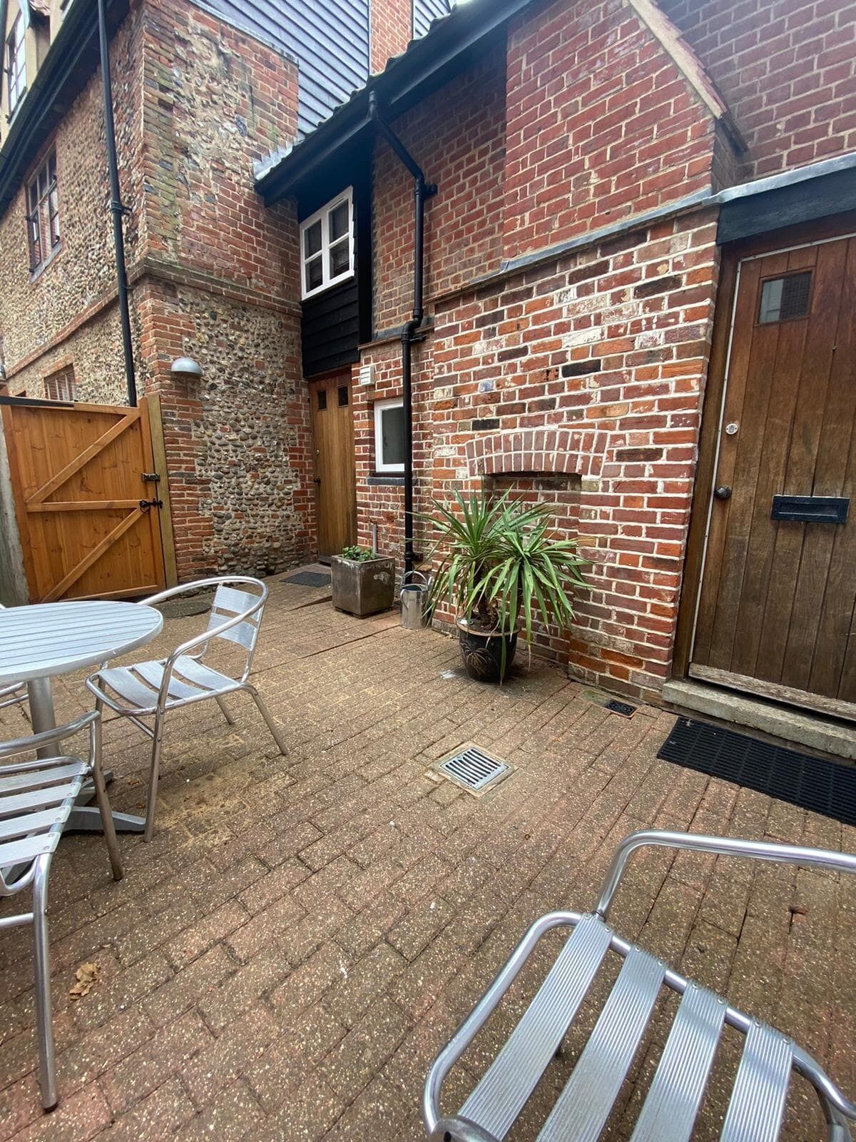 Un bâtiment en briques avec une porte en bois, un portail en métal et une petite plante en pot.