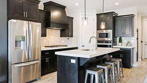 A modern kitchen with dark cabinetry, stainless steel appliances, and a central island with bar stools.