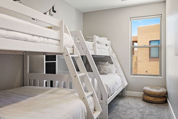 Quarto com beliche, janela, tapete pequeno e cesto de palha.