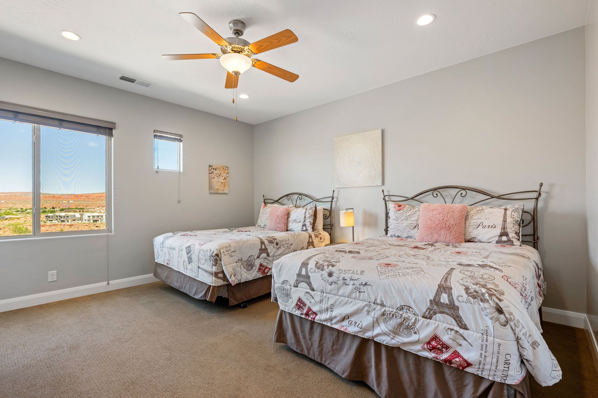 A bedroom with two beds, a ceiling fan, and a large window.