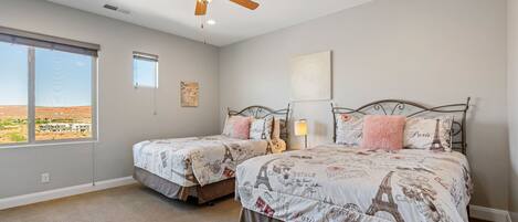 A bedroom with two beds, a ceiling fan, and a large window.
