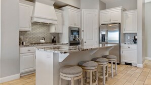 Una cocina moderna con armarios blancos, encimera de mármol y refrigerador de acero inoxidable.