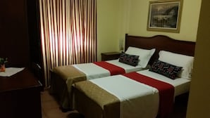 A hotel room with two single beds, a nightstand, a desk, and a window with striped curtains. - Hotel Chopin (Milan)