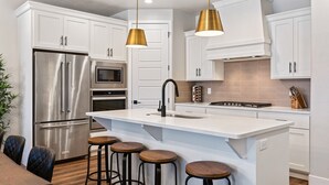 A modern kitchen with white cabinets, stainless steel appliances, and a central island with stools. - Desert Escape- Private Hot Tub! Book with next door unit! (Washington)