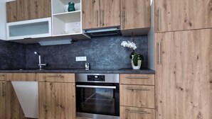A modern kitchen with wooden cabinets, a built-in oven, and a countertop with a sink and a vase with flowers. - Vacation apartment Landglück Seegraben (Bechhofen)