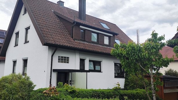 A two-story house with a sloped roof, solar panels, and a car parked in front. - Gast-und Ferienwohnung Jäger (Alfdorf)
