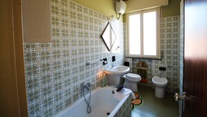 A bathroom with patterned tiles, a bathtub, a sink, a toilet, and a window providing natural light. - House Adelin (Andora)