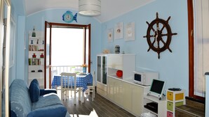 A living room with a sofa, dining table, and chairs. There is a TV, a cabinet, and a window with a view. - House Agave (Moneglia)